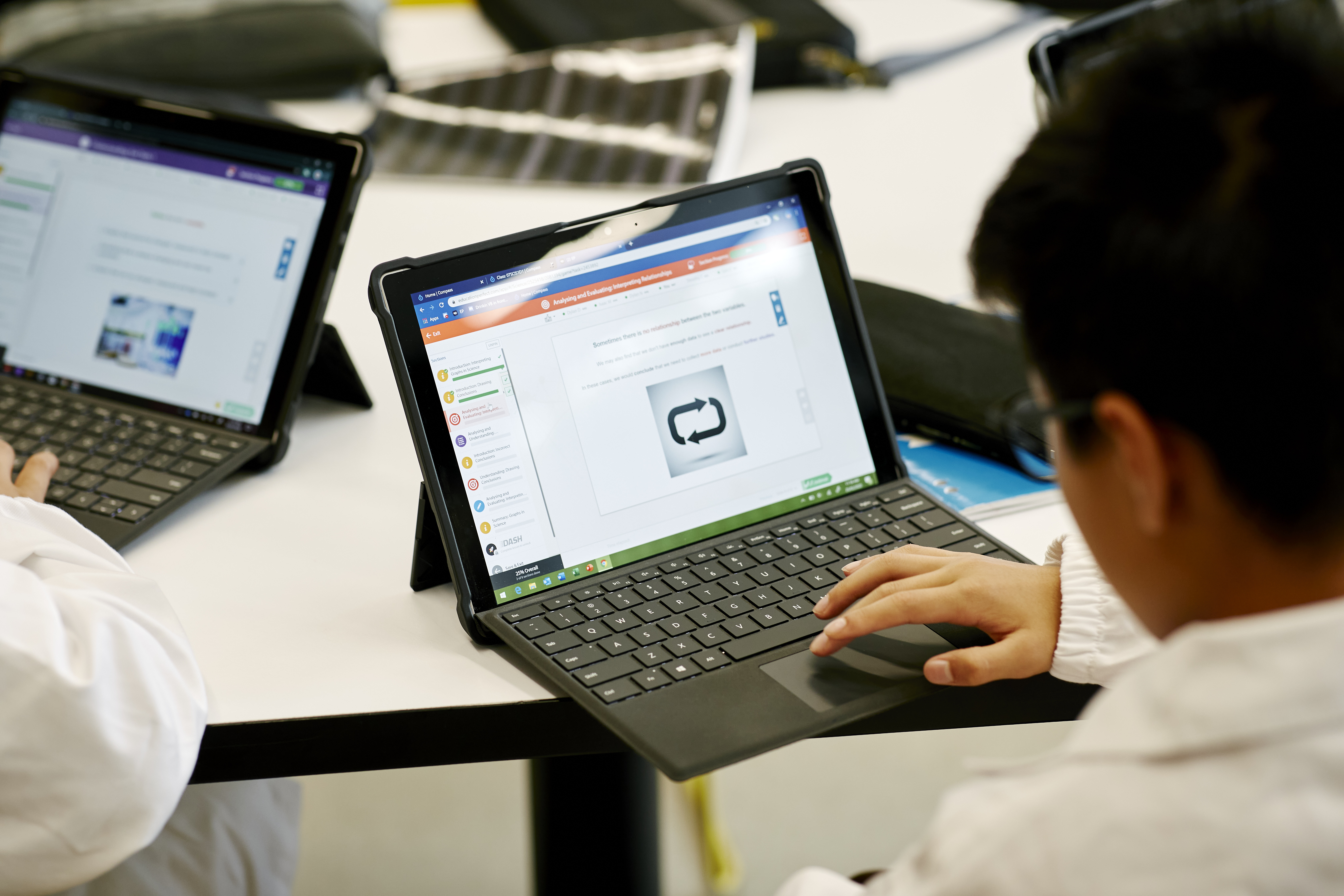 Student in a tech-enabled classroom using a tablet with a keyboard, viewing a screen with text and a curved arrow image.